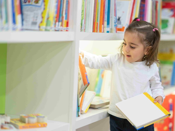 Niña escogiendo un libro en biblioteca.