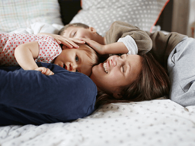 Una mujer y dos niños felices acostados en una cama.