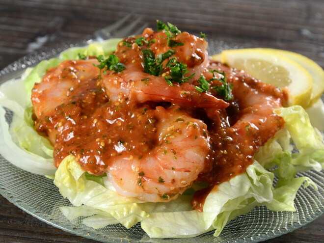 en un plato hay una base de ensalada y encima camarones con salsa