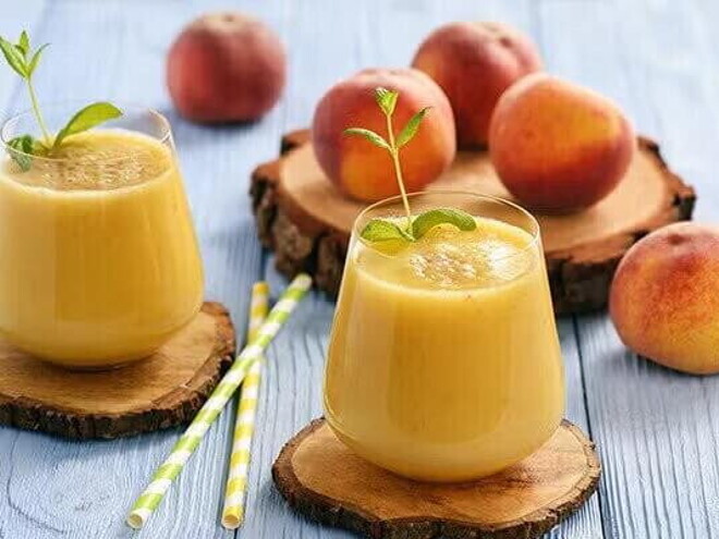 Dos licuados de naranja con durazno y frutas decorativas alrededor