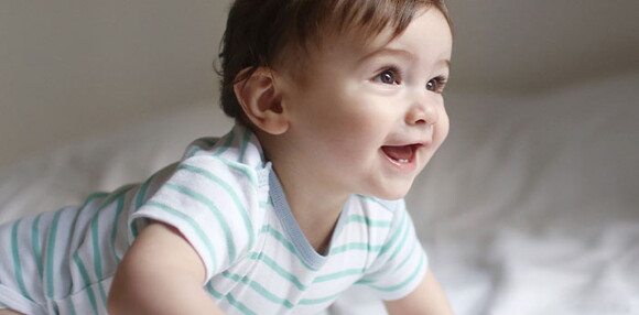 Niño sonriendo y gateando como parte del desarrollo psicomotor.